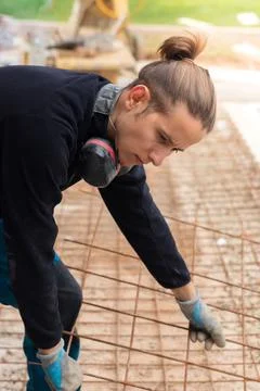Young hipster apprentice working in construction placing iron mesh grid Stock Photos