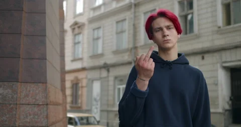 Young hipster guy with dyed red hair showing middle finger while standing at Stock Footage 143698477