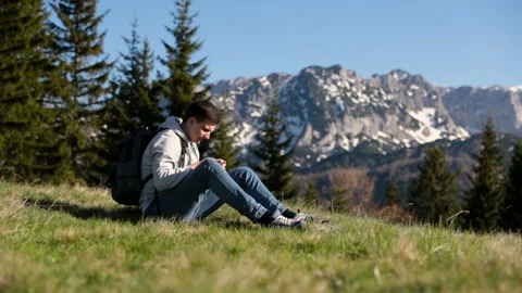Young hipster man with backpack stands on top of mountain, enjoying amazing view Stock Footage 94634081