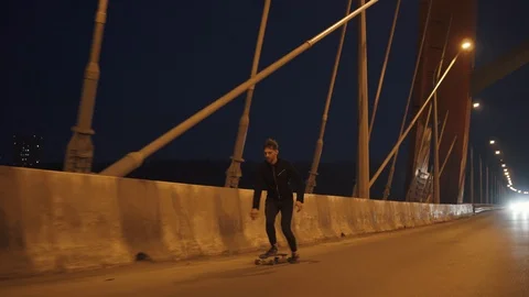 A young hipster man with a beard riding a longboard on a night city Stock Footage 89590308
