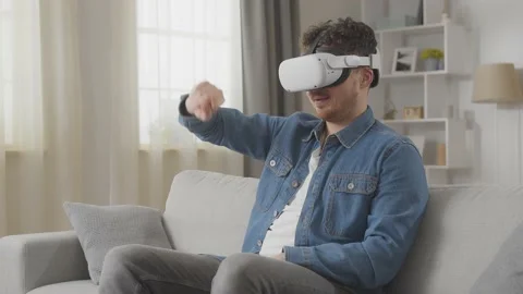Young hipster man using his VR headset for surfing the internet on sofa at home Stock Footage 169320785