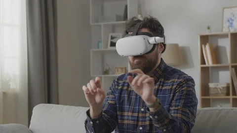 Young hipster man using his VR headset for surfing the internet on sofa at home Stock Footage 169320922