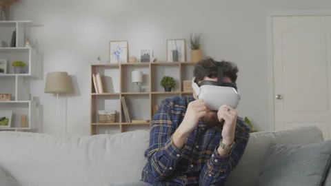 Young hipster man using his VR headset for boxing while sitting on sofa at home Stock Footage 169321022