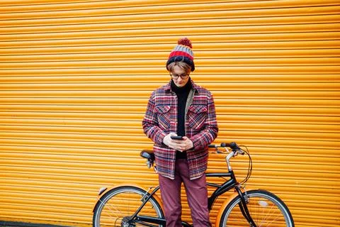 Young hipster man using mobile phone while sitting on cruiser bicycle near Foto stock