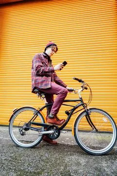 Young hipster man using mobile phone while sitting on city bicycle near orange Foto stock