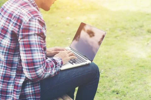 Young hipster man work on computer at the park in a sunny day. Stock Photos