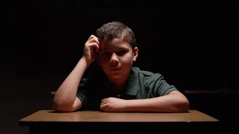 Young hispanic boy sitting at desk in the dark with a sad, lonely expression Stock Footage 141757442