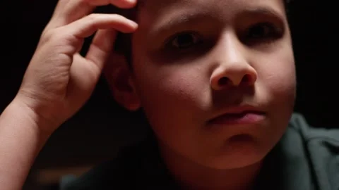 Young hispanic boy sitting at desk in the dark with a sad, lonely expression Stock Footage 141758033