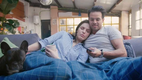 Young Hispanic couple take rest at cosy grey couch with cute pet dog on the side Stock Footage 105758644