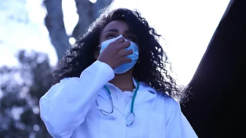 Young hispanic doctor pulls down her mask and breathes a sigh of relief Stock Footage 154174302