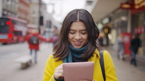 Young Hispanic female using her digital tablet as she walks through the high str Stock Footage 101067197
