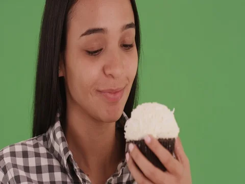 Young Hispanic girl eating a cocoanut cupcake on green screen Video stock 79256307