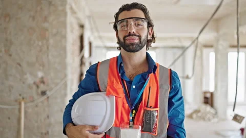 Young hispanic man architect standing with serious face holding hardhat at .. Video stock 247378255