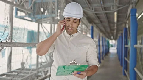Young hispanic man architect talking on holding clipboard at street Stock Footage 246125164