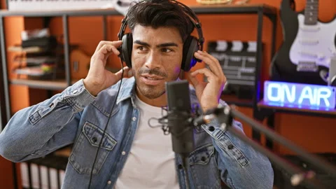 A young hispanic man with a beard adjusts his headphones in a music studio .. Video stock 268557313