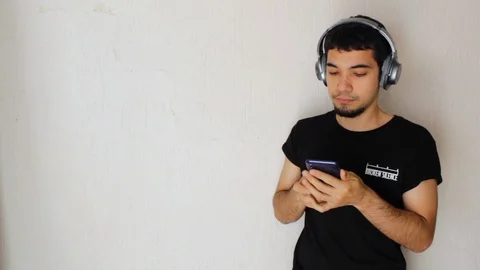 Young Hispanic man with black clothes listening to music with headphones Video stock 125885236