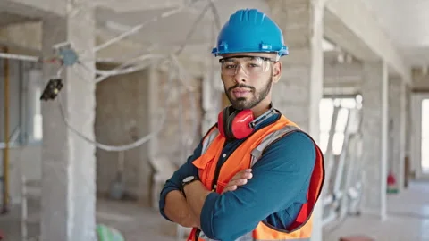 Young hispanic man builder with crossed arms wearing hardhat at constructio.. 스톡 동영상 249455198