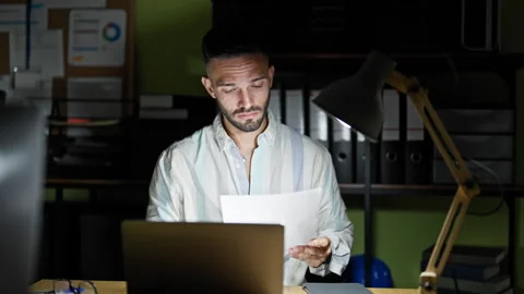Young hispanic man business worker using laptop reading document looking up.. Video stock 247382296