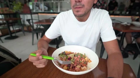Young hispanic man with cap eats salad in a restaurant Stock Footage 164654325