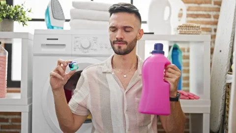 Young hispanic man choosing detergent bag or bottle at laundry room Video stock 247382260
