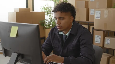 Young hispanic man at computer surrounded by parcel boxes, typing and finge.. Stock Footage 347849174