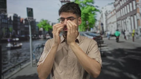 Young hispanic man covers face with both hands while standing on street bes.. Video stock 314687832