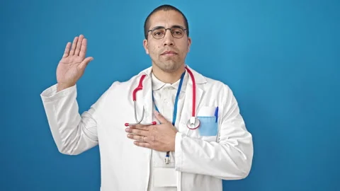Young hispanic man doctor making an oath with hand on chest over isolated b.. Stock Footage 247377333