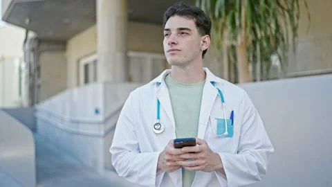 Young hispanic man doctor using smartphone at hospital Video stock 243481994