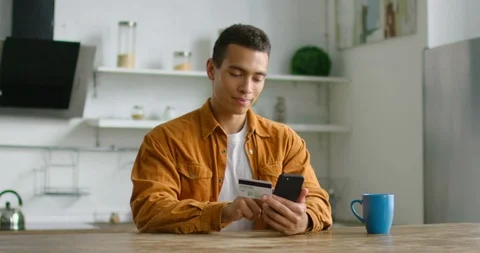 Young Hispanic man is doing online shopping in kitchen 스톡 동영상 113293032