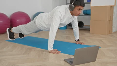 Young hispanic man doing pushup on blue mat with laptop and headphones in s.. Stock Footage 337431157