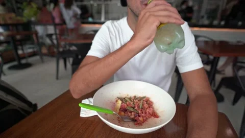 Young hispanic man drinks sparkling water while eating saladat a restaurant Stock Footage 164367525