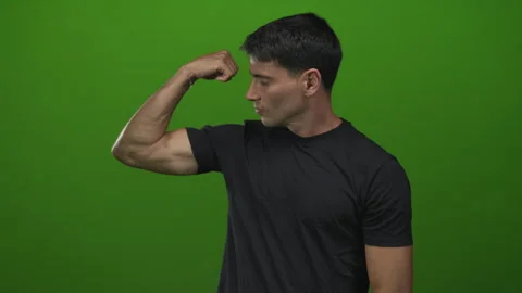 Young hispanic man flexes bicep and inspects muscle in studio against vibra.. Video stock 313464365