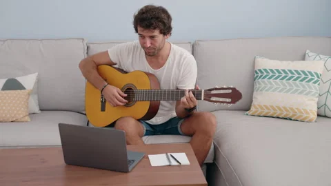 Young hispanic man having online classical guitar class sitting on sofa at ho Stock Footage 218261565