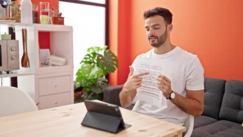 Young hispanic man having online music lesson sitting on table at dinning roo Video stock 247378869