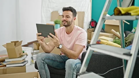 Young hispanic man having video call sitting on sofa at new home Video stock 245039391