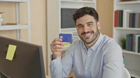 Young hispanic man holds a blue creditcard with his hand near a computer mo.. Stock Footage 339175291