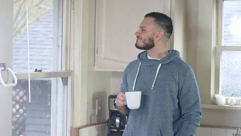 Young hispanic man laughs while enjoying morning cup of tea by kitchen window Stock Footage 84478628