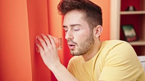 Young hispanic man listening through wall with glass at home Video stock 245044699