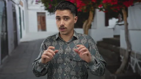 Young hispanic man looking surprised while gesturing on a city street lined.. Stock Footage 309867340