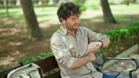 Young hispanic man looking at the watch sitting on bench with arms crossed .. Video stock 246132598