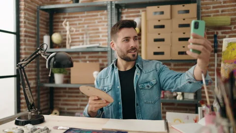 Young hispanic man make selfie by smartphone sitting on table at art studio Stock Footage 189949608