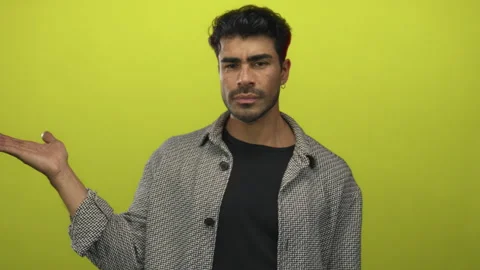 Young hispanic man in patterned jacket holds open palm and points finger in.. Stock Footage 313456973