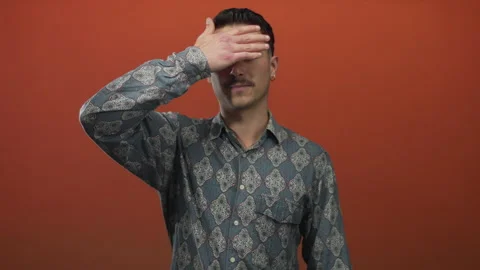 Young hispanic man in patterned shirt covers his eyes with hand against iso.. Stock Footage 315468977