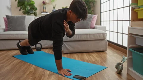 A young hispanic man performs push-ups on a blue mat in a cozy living room,.. Stock Footage 285099676