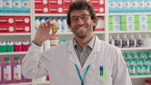 Young hispanic man pharmacist smiling confident holding pills bottle at pharm Video stock 220150463