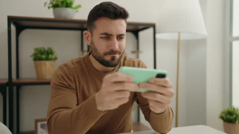 Young hispanic man playing video game by smartphone at home Video stock 173788020