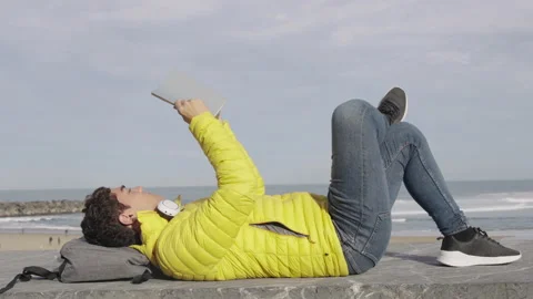 Young hispanic man reading a book at seaside Stock Footage 222569055