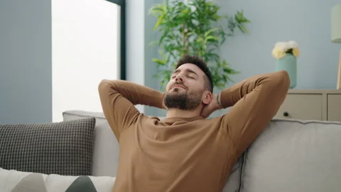 Young hispanic man relaxed with hands on head sitting on sofa at home Stock Footage 189943609