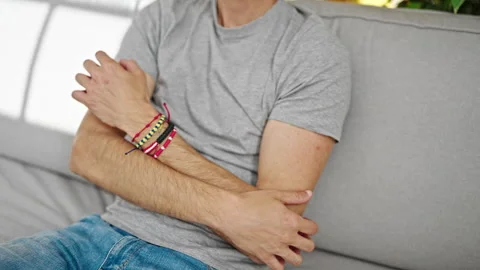 Young hispanic man scratching arm for itchy sitting on sofa at home Video stock 247384953