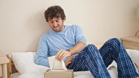 Young hispanic man sitting on bed being sick using tissue at bedroom Video stock 247379215